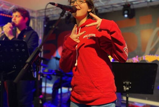 Eine Schülerin singt ins Mikrofon und macht Peace-Zeichen