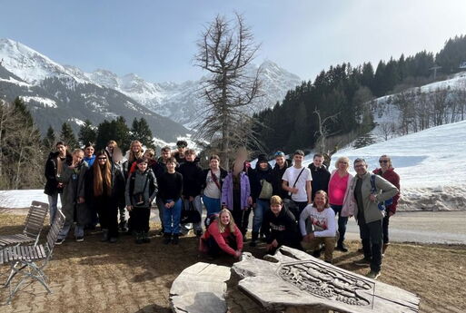 SchülerInnen und LehrerInnen stehen aufgereiht auf einer Terrasse. Hinter ihnen sieht man die verschneiten Berge.