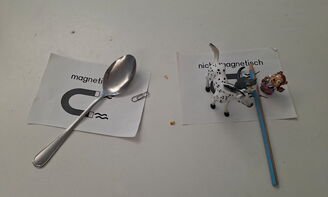 Auf einem Blatt links steht magnetisch, darauf liegen ein Löffel und eine Büroklammer, rechts liegt ein Blatt mit den Worten nicht magnetisch, darauf liegen verschiedene Gegenstände