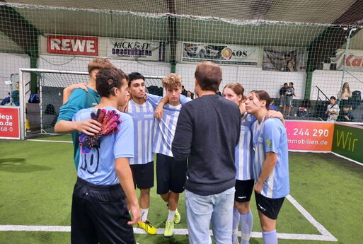 Die Schüler und Schülerinnen stehen mit ihrem Trainer im Kreis und besprechen sich.