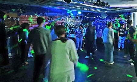 SchülerInnen und ErzieherInnen stehen auf der Tanzfläche die neue Lichtanlage leuchtet den Raum aus.