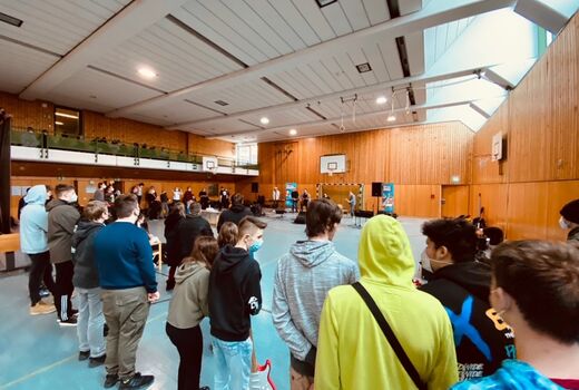 Schüler stehen in der Turnhalle und hören der Band im Hintergrund zu