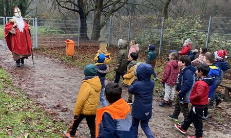 Der verkleidete Nikolaus kommt auf den Spielplatz und die Erstklässlerinnen und Erstklässler laufen ihm zur Begrüßung entgegen.