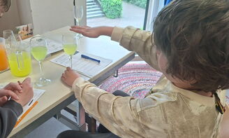 Ein Kind legt seine Finger auf ein halb gefülltes Glas auf einem Tisch, daneben steht ein weiteres halb gefülltes Glas