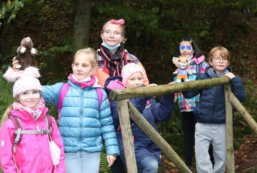 Sechs Kinder stehen auf einer Holzbrücke und halten die Maskottchen vom Freitagsclub hoch