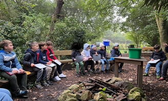 Kinder, in winterlicher Kleidung, sitzen im Freien an einer Feuerstellen.