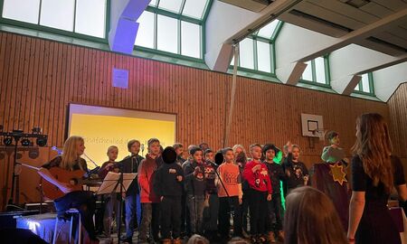 Unsere Grundschüler und Grundschülerinnen stehen auf der Bühne singen mit Frau Wagner und ihrer Gitarre das Schäfchenlied.
