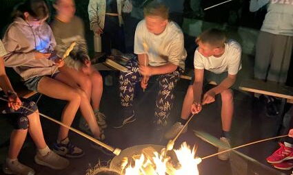 Jugendliche sitzen am Lagerfeuer und halten Stockbrot in die Glut