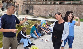 SchülerInnen und ErzieherInnen stehen und sitzen vor einem Brunnen.