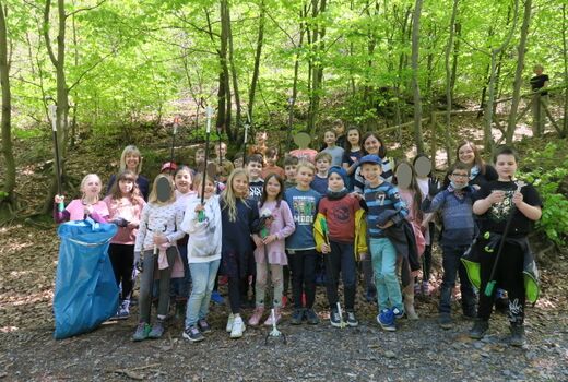 Gruppenfoto  im Wald von zwei dritten Klassen mit ihren Lehrerinnen und alle sind mit Handschuhen, Müllzangen und Mülltüten ausgestattet.