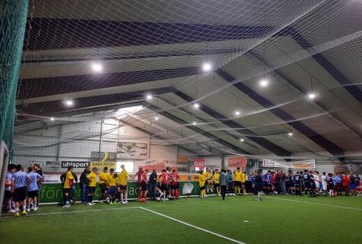 Blick in eine Sporthalle: Entlang der Bande stehen viele Schüler in Fußballtrikots und warten oder besprechen.