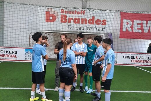 Acht SchülerInnen in Fußballkleidung stehen mit ihrem Lehrer vor dem Tor und sprechen sich ab