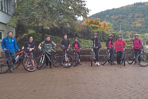 Schülergruppe mit acht Schülern und ein Lehrer stehe im Halbkreis mit den Mountainbikes auf dem Schulhof