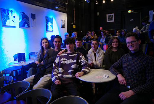 Christian Klein sitzt mit Schülerinnen und Schülern des Bildungsangebots Improtheater um einen Tisch im Improtheater Mannheim.