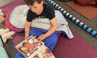 Ein Junge sitzt im Schlafsack und liest ein Comic
