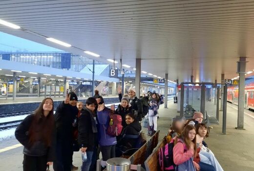 Eine Gruppe Jugendlicher sitzt am Bahnhof und wartet auf den Zug. In den Gesichtern sieht man Vorfreude auf das Landheim.