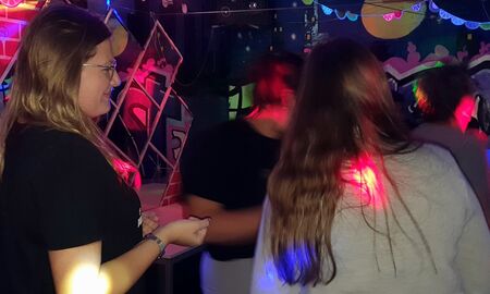 Drei Mädchen stehen auf der Tanzfläche. Eines davon ist von der Seite zu sehen. Sie lächelt.