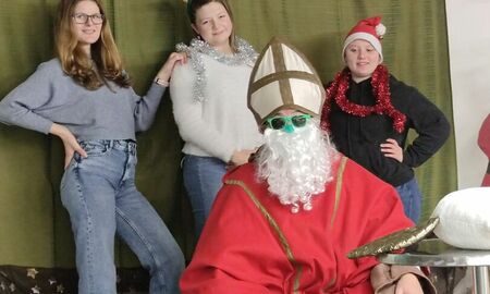 Drei Schülerinnen stehen hinter dem Nikolaus. Zwei haben Hirschgeweihe auf und eine Schülerin eine Nikolausmütze.