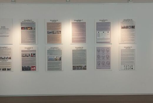 An einer Wand hängen 14 Plakate, die Informationen zu Gewalttaten gegen Menschen mit Migrationshintergrund thematisieren. Auf einem Plakat sind die neun Opfer mit Migrationshintergrund des Hanauer Attentats zu sehen.