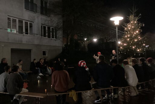 SchülerInnen und ErzieherInnen sitzen auf Bänken vor dem Weihnachtsbaum und hören der Rede des Erziehungsdienstleiters zu