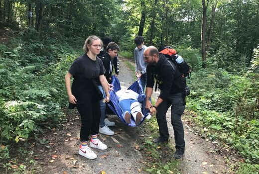 Fünf Personen tragen eine Person durch den Wald