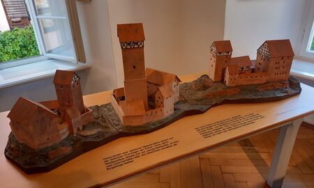 Ein kleines Modell auf einem Tisch zeigt drei mögliche Rekonstruktionen einer Burg, von der lediglich Überreste gefunden wurden.