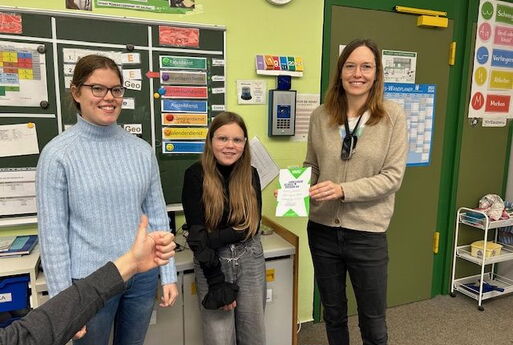Die zwei Gewinnerinnen des Vorlesewettbewerbs strahlen in die Kamera. Die Lehrerin zeigt eine Urkunde.