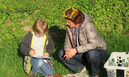 Ein Schüler löst eine Aufgabe und schreibt etwas. Neben ihm ist eine Erzieherin