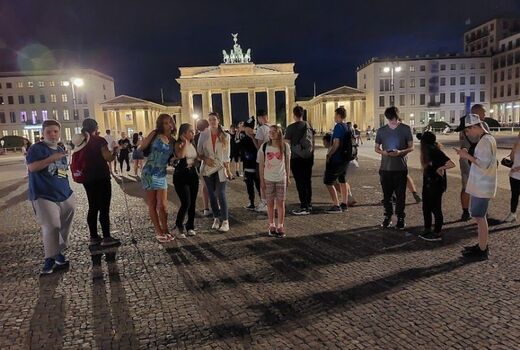 Zwölf Schüler stehen im Halbrund um den Fotografen. Manche schauen in die Kamera. Im Hintergrund sieht man das beleuchtete Brandenburger Tor.