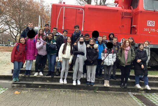 Eine Gruppe Schüler und Schülerinnen der siebten Klassen steht auf Treppenstufen vor einer roten Lok