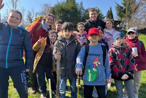 Zehn Jungs und Mädchen aus der dritten Klasse mit einer Lehrerin und einem Lehrer stehen draußen und lächeln in die Kamera