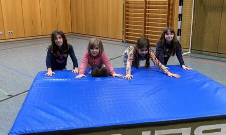 Kinder schieben in einer Turnhalle eine Weichbodenmatte