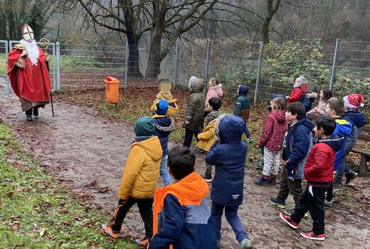 Der verkleidete Nikolaus kommt auf den Spielplatz und die Erstklässlerinnen und Erstklässler laufen ihm zur Begrüßung entgegen.