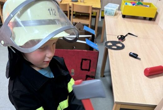 Ein Junge in Feuerwehrmontour arbeitet mit einem Spielzeugbeil.