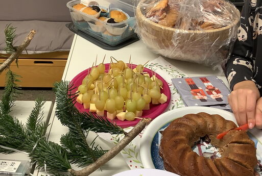 Ein Buffet aus verschiedenen Speisen, wie ein Kuchen, der gerade angeschnitten wird, Muffins und Käse-Weintrauben-Spieße