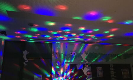 Ein dunkles Klassenzimmer wird von vielen bunten Lichtflecken einer Diskokugel erleuchtet.