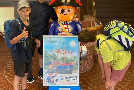 Drei Schüler stehen neben einer großen Playmobil-Figur.