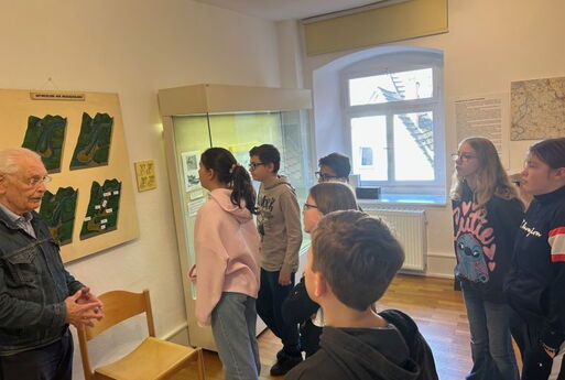 Ein älterer Herr erklärt den SchülerInnen etwas. Sie blicken zu einem Relief der Neckarschleife.