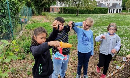 Vier Kinder zeigen mit dem Daumen nach unten. Ein Kind hält eine Maske in der Hand