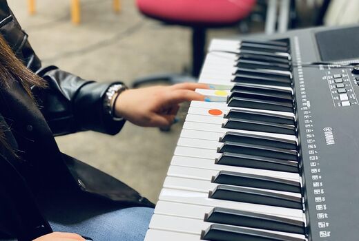 Eine Schülerin spielt auf einem Keyboard, das Keyboard hat gelbe und rote Markierungen
