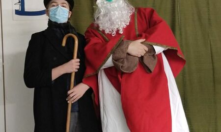 Ein Schüler steht neben dem Nikolaus. Der Schüler hat einen Zylinder auf und einen Stock in der Hand.