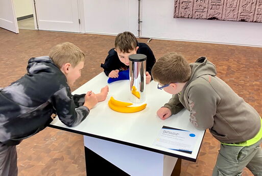 Drei Jungs stehen um einen Tisch und schauen sich eine Säule an.