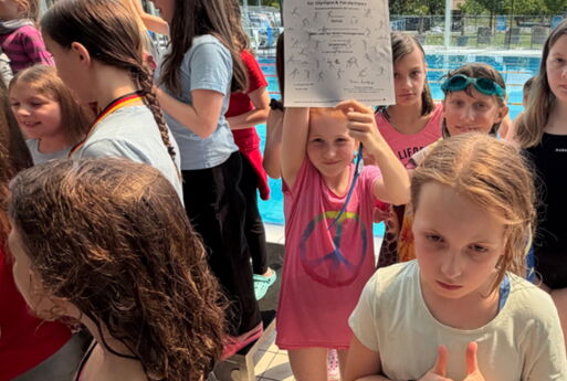Viele Mädchen stehen vor dem Schwimmbecken, ein Kind hält ihre Urkunde in die Kamera