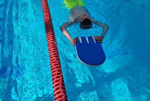 Ein Junge schwimmt auf dem Rücken mit einem Schwimmbrett im Schwimmbecken