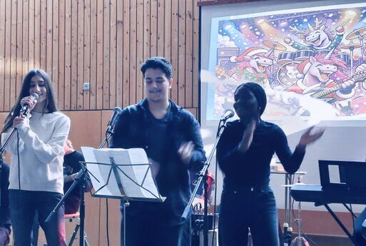 Drei SchülerInnen singen und klatschen auf einer Bühne