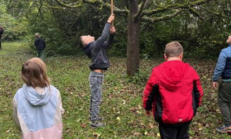 Ein Junge holt mit einem Staab einen Apfel vom Baum. Andere Kinder schauen zu.