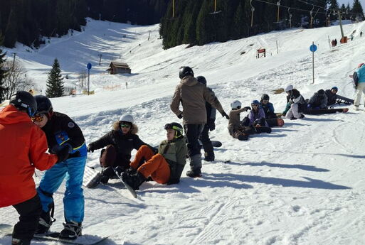 Die Snowboarder sitzen hintereinander im Schnee.