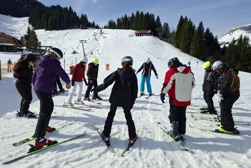 Zwölf junge SkifahrerInnen stehen im Kreis am Fuße einer Skipiste
