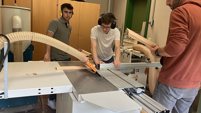 Zwei Schüler sägen unter Anleitung an der Sägemaschine.